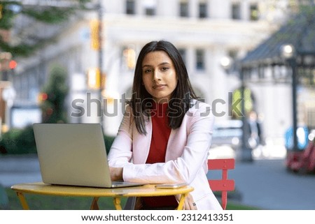 Portrait of young confident Indian businesswoman, freelancer using laptop computer looking at camera, working online sitting at workplace. Successful business  Royalty-Free Stock Photo #2312413351
