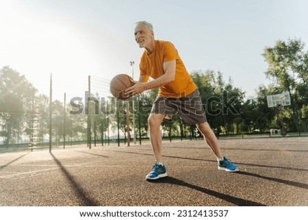 View from the bottom. Caucasian handsome motivated strong senior male athlete playing basketball at outdoors summer court. People. Competitive sports games. Active healthy lifestyle in retirement