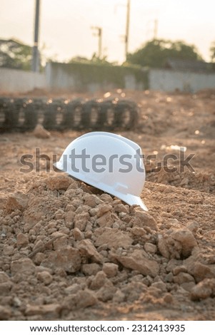 A white safety hardhat helmet is placed on dirt ground at the construction work site, unsafe workplace. Safety PPE object photo. 