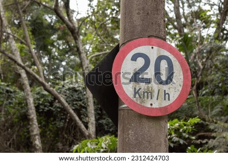 Photograph of 20 kilometers per hour speed limit sign with trees in the background.
