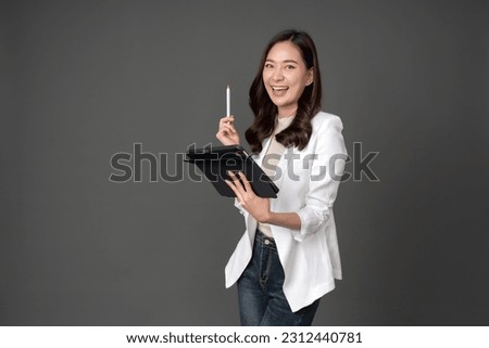 Asian female executive with long hair is happy. She uses a tablet and pen to conduct business. wearing a white suit and stand to take pictures with a gray scene in the studio