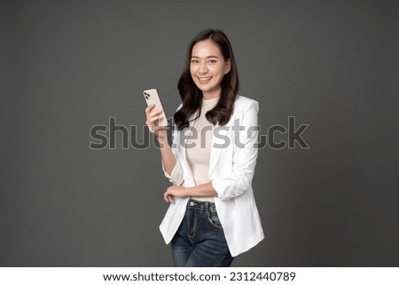 Asian female executive with long hair smile brightly and hold the phone confidently wearing a white suit Standing and taking pictures against the gray background in the studio