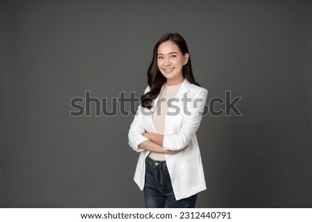 Asian female executive with long hair She smiled brightly and confidently stood with her arms crossed. She wore a white suit. and stand to take pictures with a gray scene in the studio Royalty-Free Stock Photo #2312440791