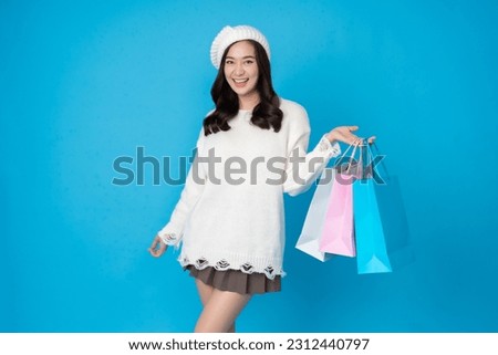 Asian woman shopaholic with long hair Take pictures in the blue studio scene smile brightly In her left hand are several shopping bags. Wear a white coat, hat and skirt.