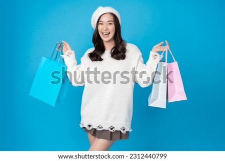 Asian woman shopaholic with long hair Take pictures in the blue studio scene laughing and smiling In her right hand and left hand are shopping bags. Wear a white coat, hat and skirt.