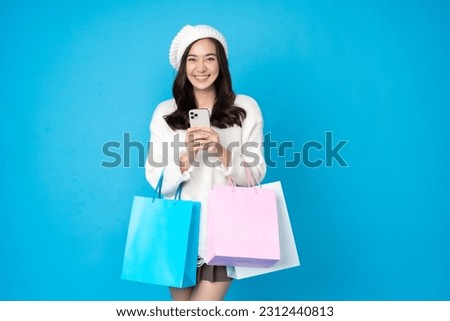 Asian woman shopaholic with long hair Take pictures in the blue studio scene using a mobile phone happy smile There is a shopping bag hanging on his hand. Wear a white coat, hat and skirt.