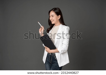Asian female executive with long hair smiling beautifully Holding a tablet at work and pointing a pen to a destination wearing a white suit and stand to take pictures with a gray scene in the studio