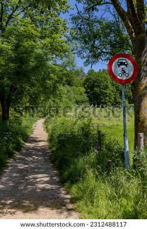 Hiking trail with traffic signs: prohibited cars and motorcycles in Dutch nature reserve Bemelerberg, forbidden access, abundant leafy trees and wild vegetation, sunny day, South Limburg, Netherlands