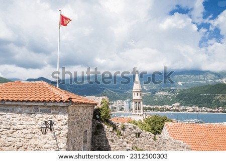 Montenegro flies proudly above Budva old town next to churches and medieval buildings pictured in May 2023.