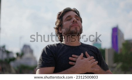 Tranquil young man putting hand in chest taking a deep breath outside at park feeling peace of mind Royalty-Free Stock Photo #2312500803
