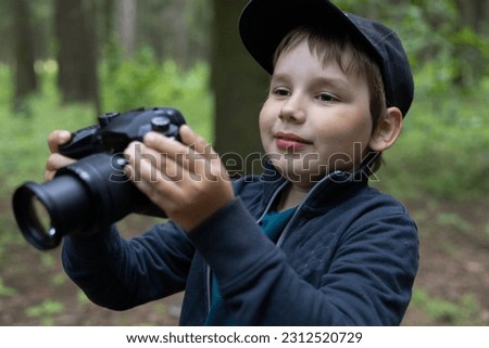 In the forest, a child with a camera photographs beautiful wildlife. A child learns to take pictures with a camera in a summer forest of magical nature. Child boy loves to take pictures.