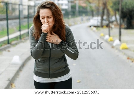 Young sporty woman coughing while walking on the street. Athlete woman affected by air pollution during running training Royalty-Free Stock Photo #2312536075