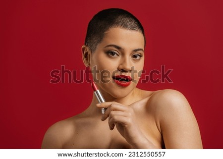 Beautiful young short hair woman holding lipstick against red background