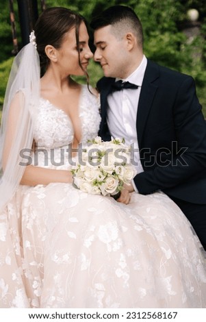 Groom and bride sits on bench and hug each other. Focus on bouquet 