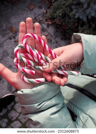 Christmas lollipops in white with red and green flowers hold baby hands of a girl in a grey jacket top view . Christmas . hands of a person 