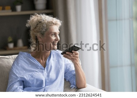 Happy senior mature lady talking on speaker on cellphone call, speaking at dynamic, holding smartphone at face, recording audio message, resting at home, smiling, laughing, enjoying communication Royalty-Free Stock Photo #2312624541