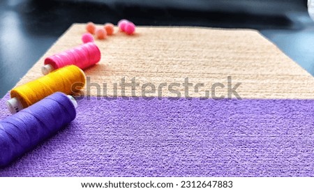 Abstract background with texture and frame with beige, lilac or purple velvet paper and colour pink, yellow, blue spools of thread with colored soft fluffy balls. Top view. Partial focus