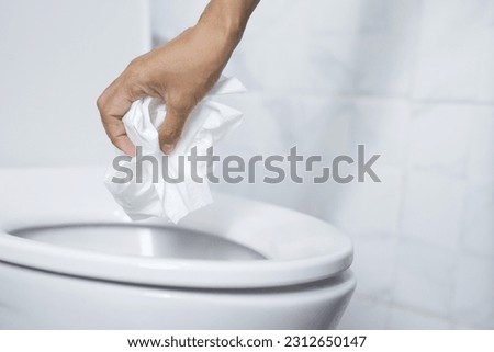 close up hand holding a tissue to be thrown into the toilet bowl. Can not drain water of toilet paper in the toilet bowl cause the stool to clog up. Royalty-Free Stock Photo #2312650147