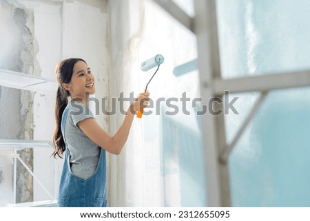 Asian attractive Young asian woman smiling cheerful happy female painting new home interior wall with paint roller in new house, Home relocation and renovation decoration daytime concept Royalty-Free Stock Photo #2312655095