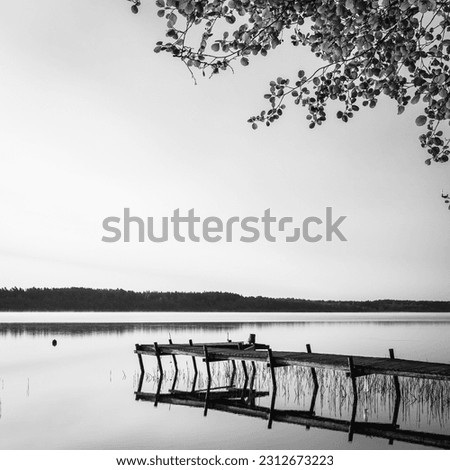 Black and white  landscape photography of Latvia countryside. Sunrise by the lake with old wooden pier and water reflection.