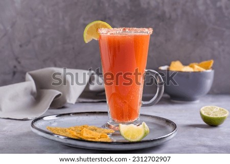 Michelada cocktail with tomato juice, beer and lime in a glass and nachos