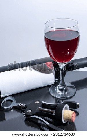 A glass of red wine with a bottle and a corkscrew beside it