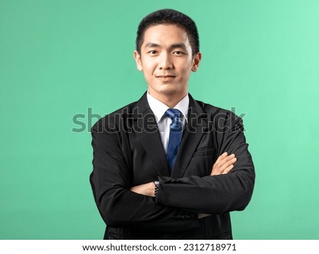 A portrait of an Asian man wearing a white shirt and a black suit, while folding his hands, isolated on a green background.
