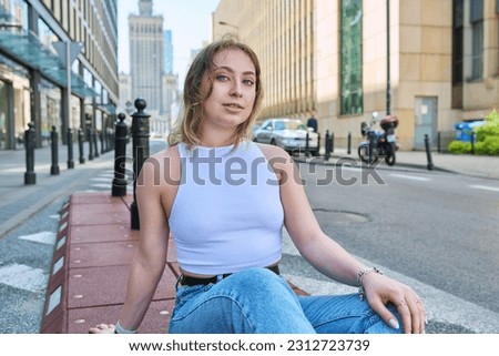 Young beautiful girl 19, 20 years old sitting on sidewalk, modern urban style