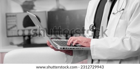 Side view portrait of young doctor with laptop in his hospital cabinet. Monitor with brain image in the background.