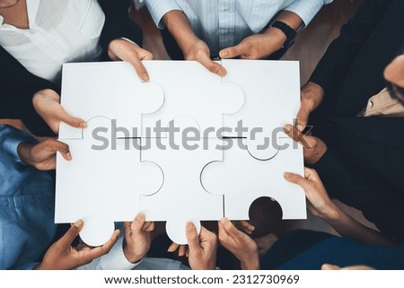 Diverse corporate officer workers collaborate in office, connecting puzzle pieces to represent partnership and teamwork. Unity and synergy in business concept by merging jigsaw puzzle. Concord Royalty-Free Stock Photo #2312730969