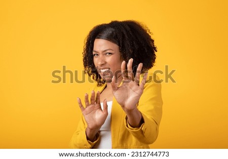 Displeased young african american lady making stop gesture with hands, push back camera, isolated on yellow background, studio. Disgust, sign of personal space, say no and negative emotion