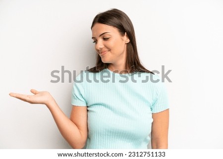 young adult pretty woman feeling happy and smiling casually, looking to an object or concept held on the hand on the side