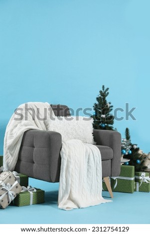 Beautiful Christmas themed photo zone with stylish armchair, trees and gift boxes on light blue background