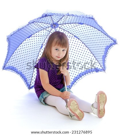 Very cheerful little girl sits under a blue umbrella. Happy childhood, fashion, autumnal mood concept. Isolated on white background
