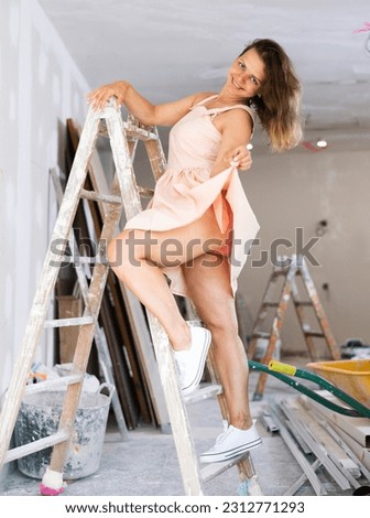 Attractive young woman wearing dress, posing in construction site, standing on stepladder.