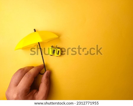 Someone hand holding yellow umbrella covered yellow car on a yellow background