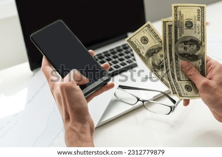 Mixed race man in glasses working with multiple electronic internet devices. Freelancer businessman has tablet and cellphone in hands and laptop on table with charts on screen. Multitasking theme