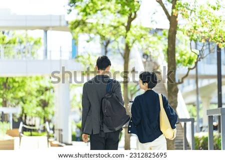An Asian couple is walking along a stylish street surrounded by fresh greenery. Royalty-Free Stock Photo #2312825695