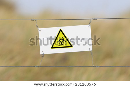 Border fence - Old plastic sign with a flag - Biohazard