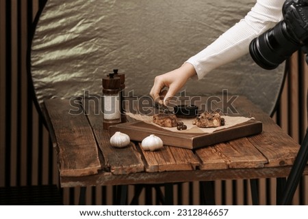 Food stylist creating beautiful composition with meat medallions on wooden table in photo studio, closeup
