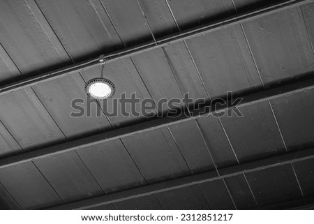 LED floodlight lamp on black metal ceiling on the factory warehouse place. Industrial building equipment object, selective focus.