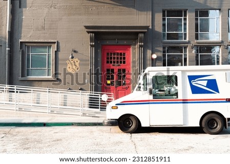 Industrial building with a red door and a US postal service truck parked out front Royalty-Free Stock Photo #2312851911