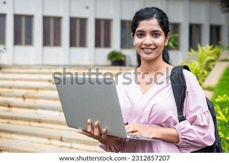 Confident girl student with backpack holding laptop by looking at camera at college campus - concept of education, technology and development
