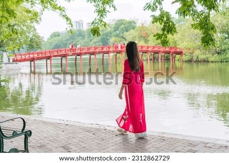 Rear view of young Asian woman tourist wearing Ao Dai (traditional Vietnamese dress) sightseeing at the Red Bridge in Hoan Kiem Lake, Hanoi, Vietnam. Copy space Royalty-Free Stock Photo #2312862729