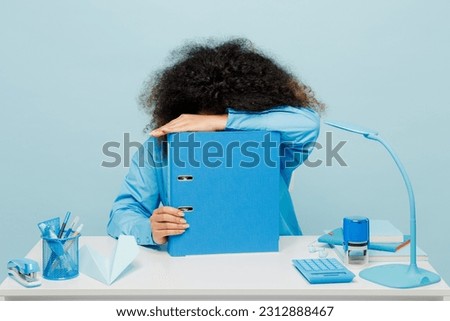Young sad tired employee business woman wearing casual shirt sit work at white office desk put head on folder for papers document bookkeeping isolated on plain pastel blue background studio portrait