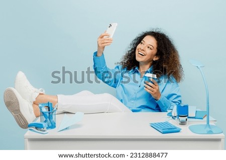 Full body young employee business woman wear casual shirt work sit on white office desk drink coffee do selfie shot on mobile cell phone isolated on plain pastel light blue background studio portrait