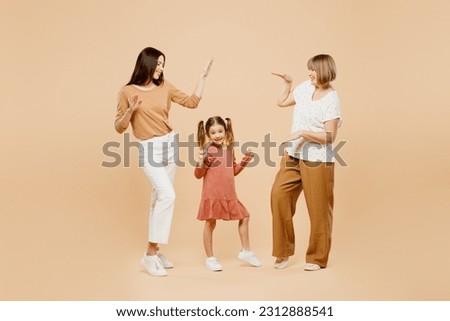Full body smiling happy women wear casual clothes with child kid girl 6-7 years old. Granny mother daughter dance on party raise up hands isolated on plain beige background. Family parent day concept