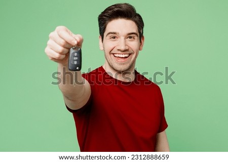 Young overjoyed man he wears red t-shirt casual clothes hold in hand car fob keyless system stretch hand to camera isolated on plain pastel light green background studio portrait. Lifestyle concept