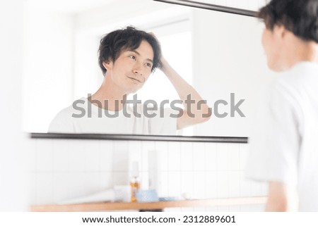 Japanese man doing hair styling while looking in the mirror Royalty-Free Stock Photo #2312889601