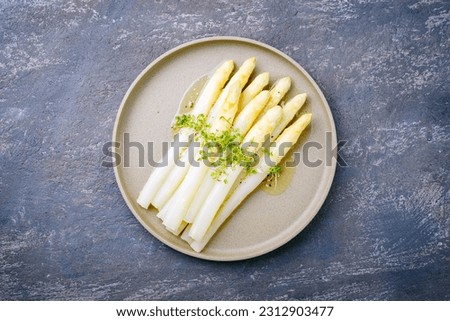Modern style traditional steamed white asparagus with butter sauce hollandaise and cress served as top view on a Nordic design plate with copy space Royalty-Free Stock Photo #2312903477